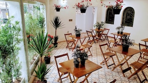 An indoor dining area with multiple wooden tables and chairs, surrounded by potted plants and a patterned floor. - Deck Hostel Congonhas (São Paulo)