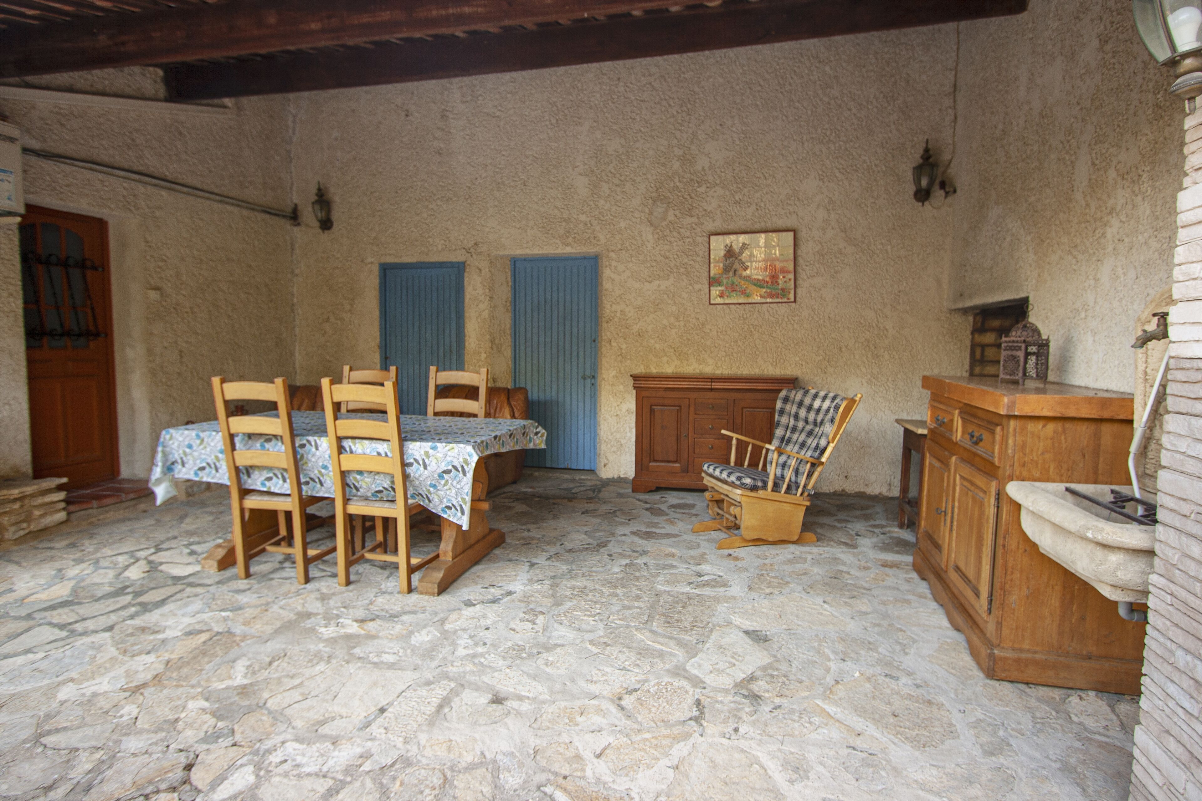 Ein Zimmer mit Steinfußboden, einem Holztisch, Stühlen, einer Bank und einem Schrank.