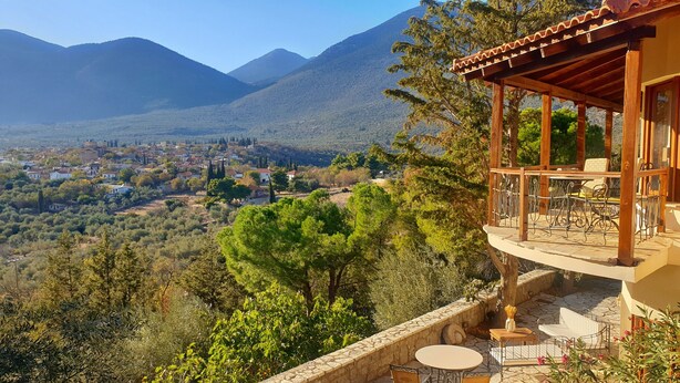 Un balcon en bois, adossé à un mur de pierre, qui offre une vue sur un paysage montagneux avec un village en contrebas.