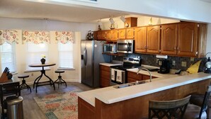 A kitchen with wooden cabinets, a refrigerator, a microwave, a stove, a sink, and a small dining area with a table and chairs. - Peaches and Beaches.... come eat some fresh peaches, close to the island beaches (Saint Marys)
