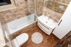 Een moderne badkamer met een glazen douchecabine, een wit bad, een wastafel met spiegel en een toilet.