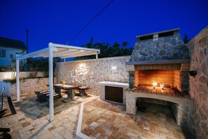 Een terras buiten met een stenen open haard, een pergola en een stenen muur.
