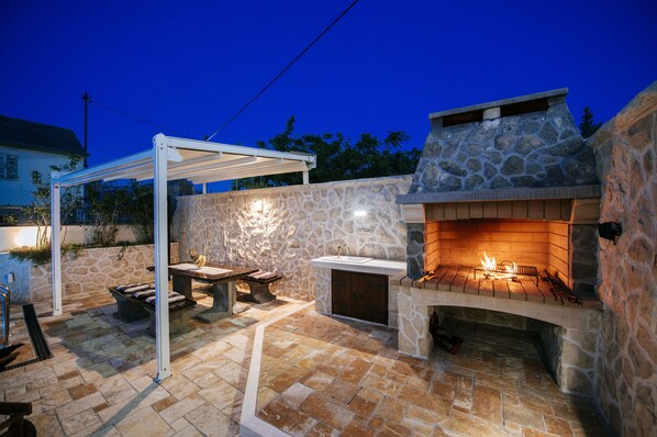 An outdoor patio with a stone fireplace, a pergola, and a stone wall.