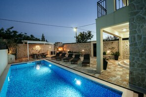 A swimming pool with lounge chairs, stone walls, and a stone building with a balcony.