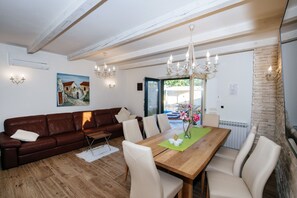 A dining area with a wooden table, beige chairs, a brown leather sofa, and a chandelier.