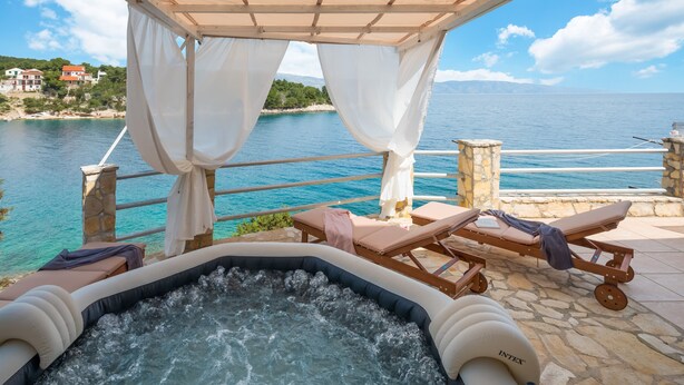 A hot tub with a view of the sea, lounge chairs, and a stone balustrade. - Apartments Habek (Jelsa)