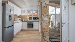 A modern kitchen with white cabinets, a stainless steel refrigerator, and a stone wall. - Apartments Habek (Jelsa)