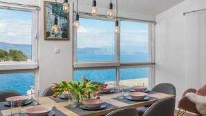 A dining area with a view of the sea, a table set with pink bowls and plates, and a vase with flowers. - Apartments Habek (Jelsa)