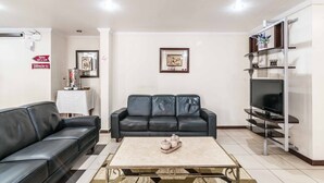Sala de estar com sofá de couro preto, mesa de centro com objetos decorativos, televisão de tela plana em um suporte e quadro pendurado na parede.