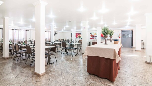 Uma ampla área de refeições interna, com várias mesas e cadeiras, pilares brancos e piso ladrilhado.