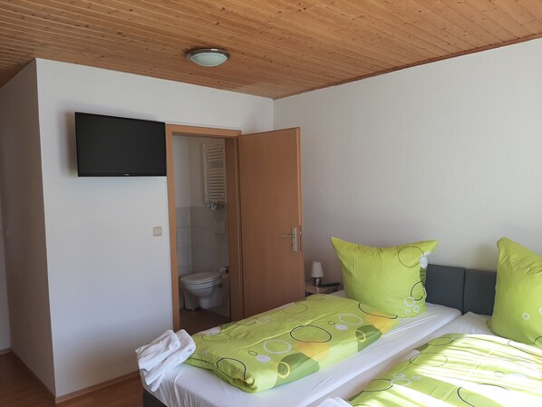 Une chambre à coucher avec un lit, un téléviseur fixé au mur et une porte donnant sur une salle de bain.