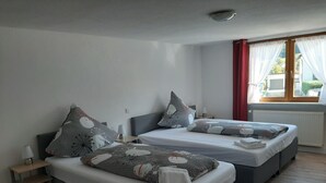 Habitación de hotel con dos camas, una mesita de noche con lámpara, un radiador y una ventana con cortinas.