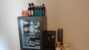 Un miniibar con dispensador de bebidas y una cafetera sobre una encimera blanca.