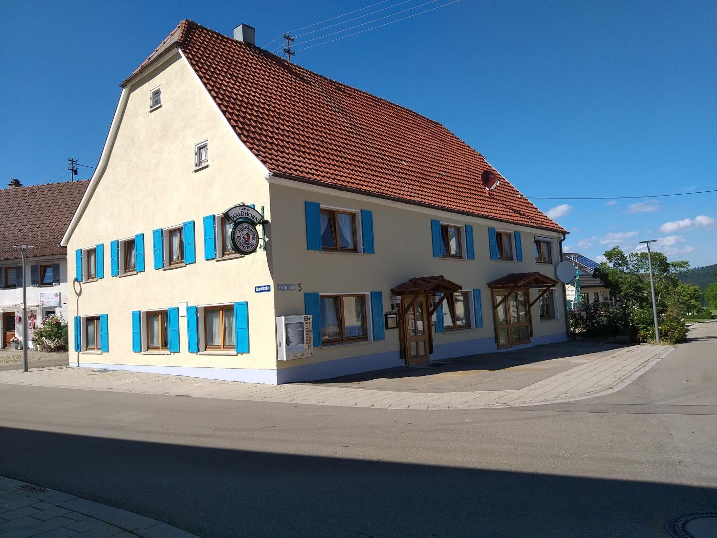 A two-story building with a red-tiled roof, blue shutters, and a sign indicating it is a restaurant.