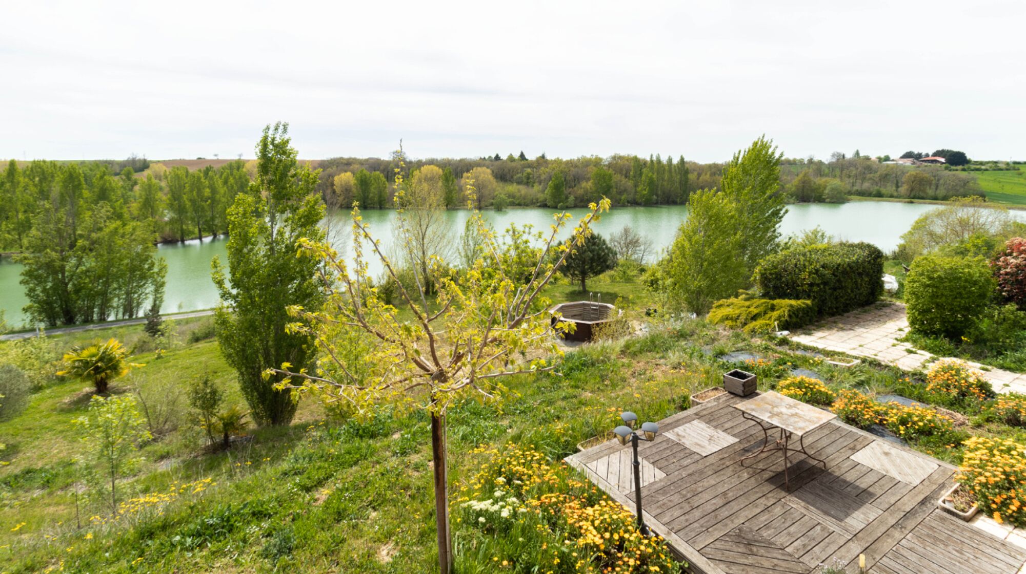 Un jardin agrémenté d’une terrasse en bois, d’un bassin et de diverses espèces d’arbres et d’arbustes.
