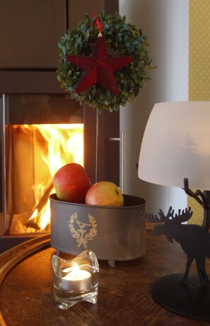 A cozy room with a lit fireplace, a candle holder with apples, a decorative star, and a moose figurine. - Inselferien Micheel (Fehmarn)