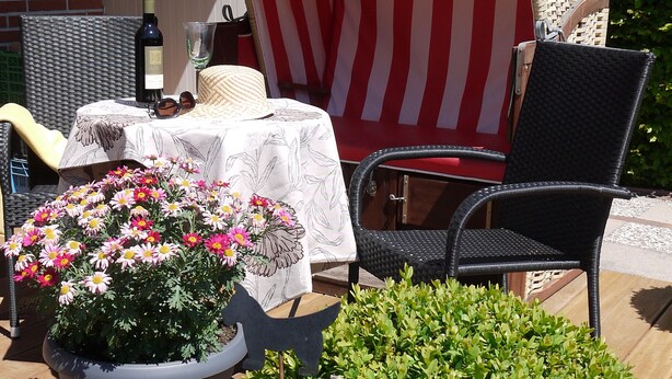A patio area with outdoor furniture, a table with a tablecloth, a potted plant, and a small structure with a striped awning. - Inselferien Micheel (Fehmarn)