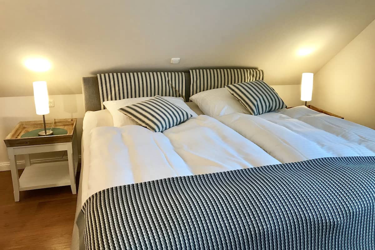 Una cama bien hecha con ropa de cama a rayas, una mesita de noche con lámpara y una mesita auxiliar de madera.
