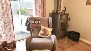 A cozy living room with a brown leather armchair, a fluffy rug, a fireplace with a deer figurine, and a black bag on the floor. - Inselferien Micheel (Fehmarn)