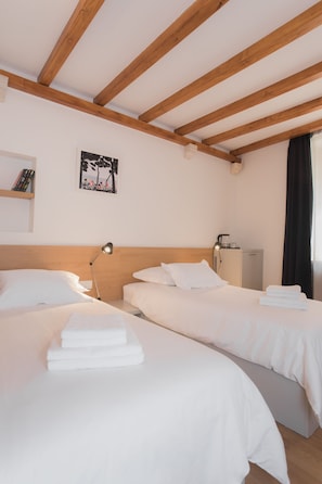 A hotel room with two beds, wooden beams on the ceiling, a small desk with a lamp, and a picture on the wall. - Rooms Kala (Sibenik)
