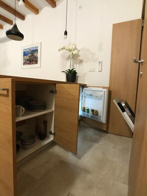 A compact kitchen with wooden cabinets, a refrigerator, and a potted orchid. - Rooms Kala (Sibenik)