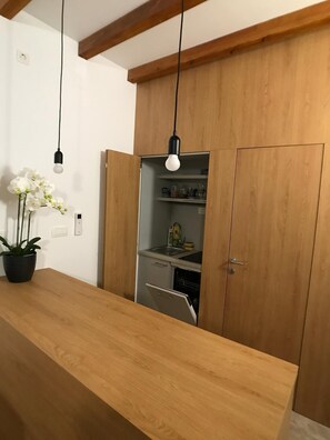 A kitchen with wooden cabinets, a countertop, and hanging pendant lights. - Rooms Kala (Sibenik)