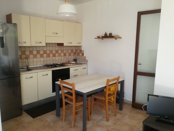 A compact kitchen with a refrigerator, stove, sink, and a dining table with chairs. - Villa Serena - Torre Inserraglio Nardò (Nardò)