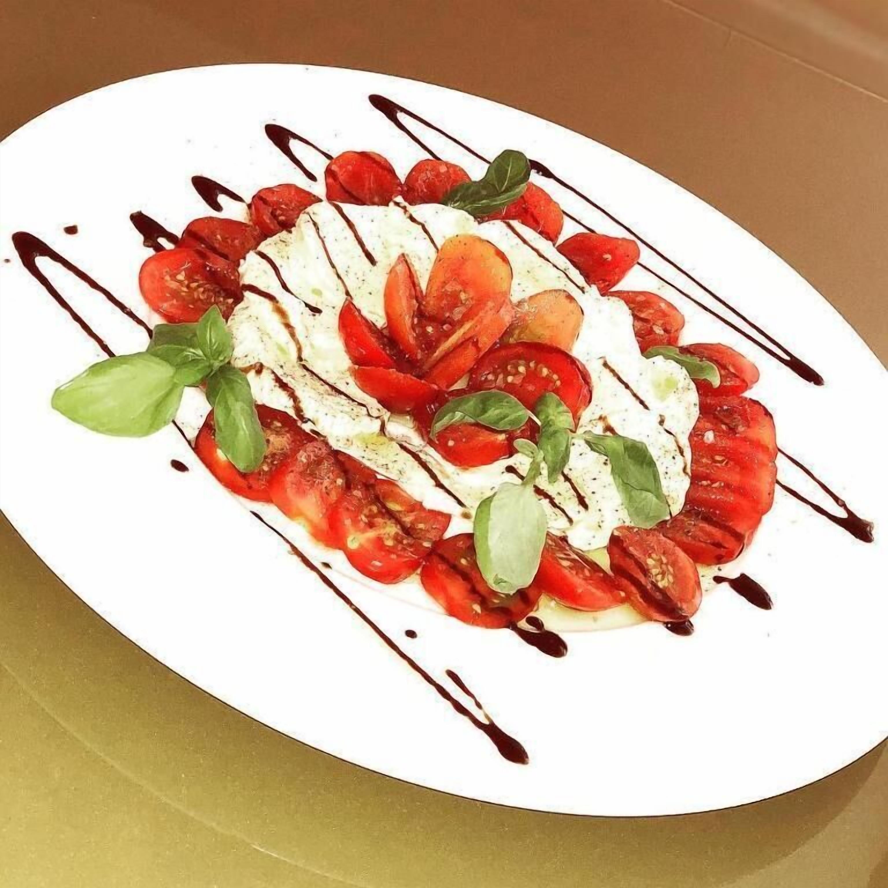 A plate of Caprese salad with tomatoes, mozzarella, and basil, drizzled with balsamic glaze.
