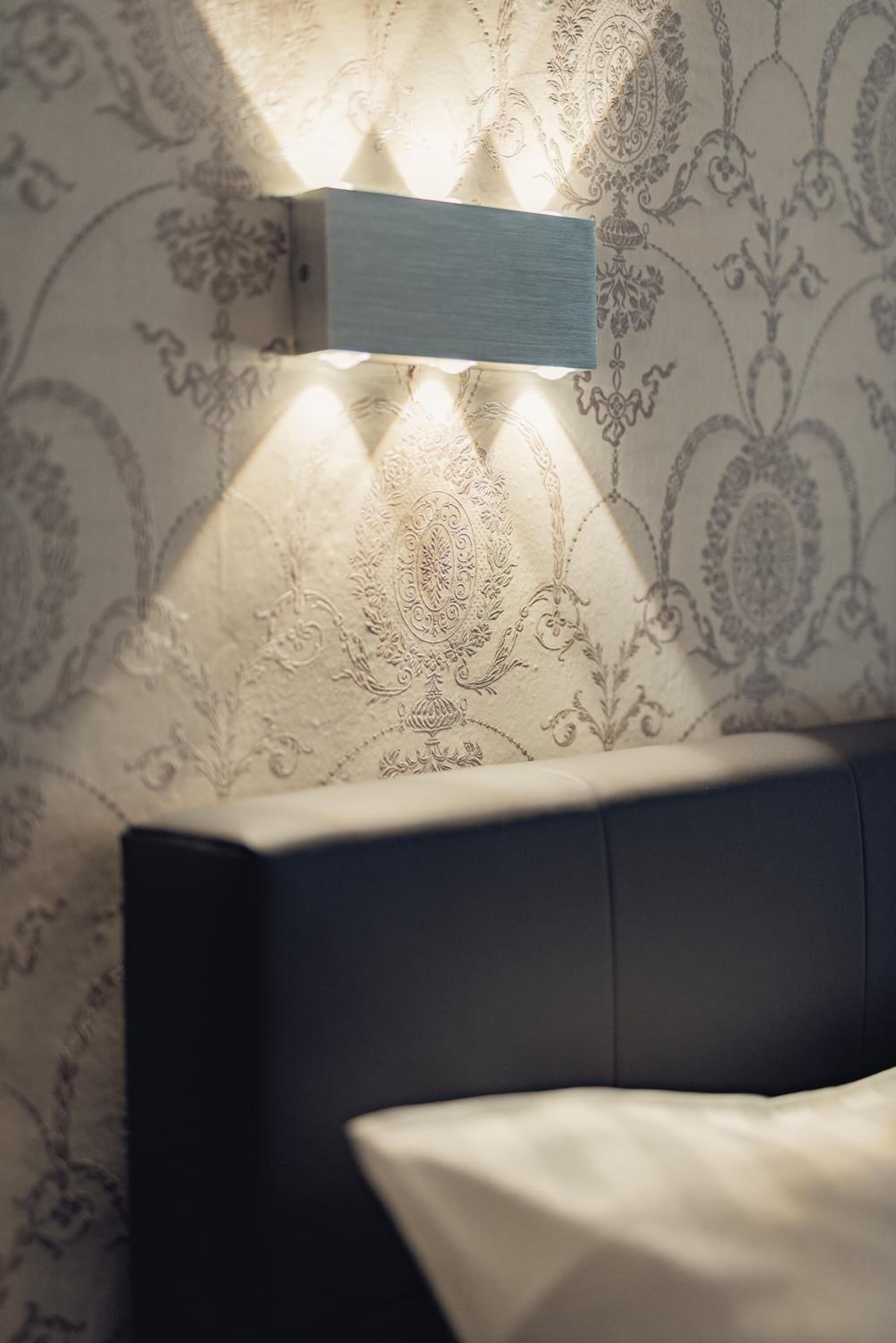 A modern room with a dark headboard, patterned wallpaper, and a wall-mounted light fixture.