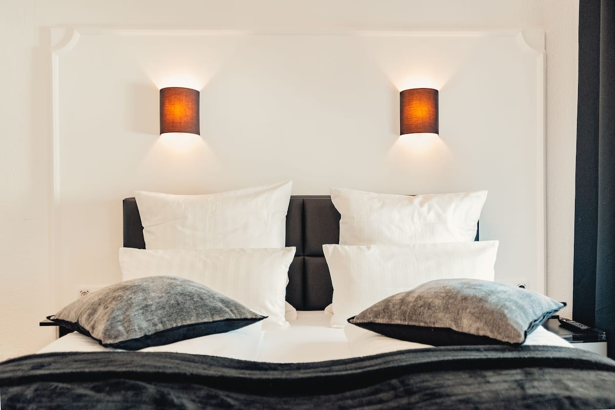 A bed with white and grey pillows, a black headboard, and two wall-mounted lights.