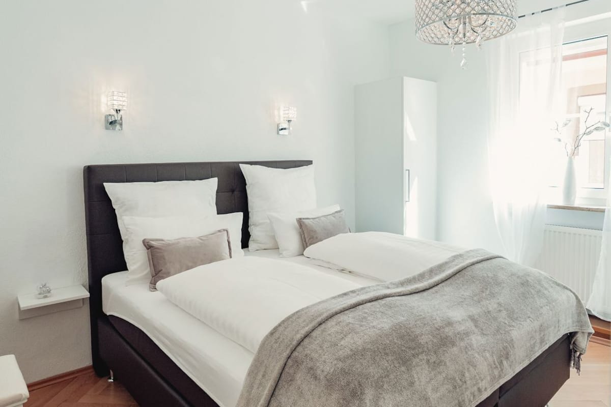 A modern bedroom with a bed, bedside tables, a hanging light fixture, and a view of the outside.