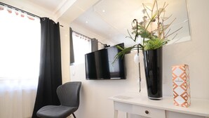 Une chambre moderne équipée d’un téléviseur à écran plat, d’un fauteuil noir, d’un bureau blanc, d’une plante en pot et d’une boîte à l’effigie de Ferrari.