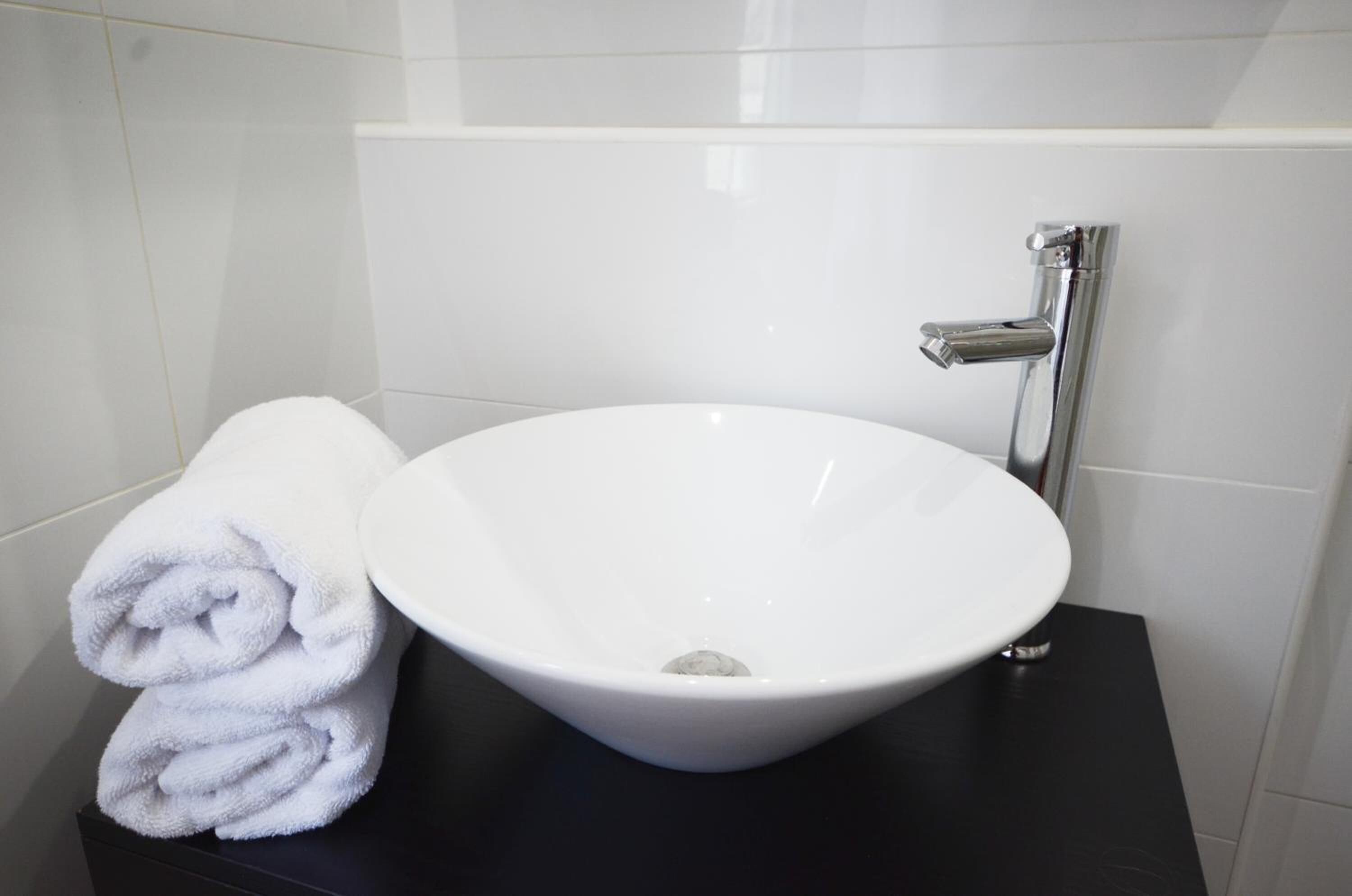 A white ceramic sink with a modern faucet on a black countertop in a bathroom with white tiled walls.