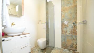 Een moderne badkamer met een wit wastafel, een toilet en een douchecabine met glazen wanden.