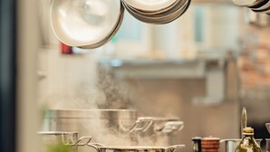 Une cuisine avec des casseroles et des poêles en acier inoxydable suspendues au-dessus d’une cuisinière.