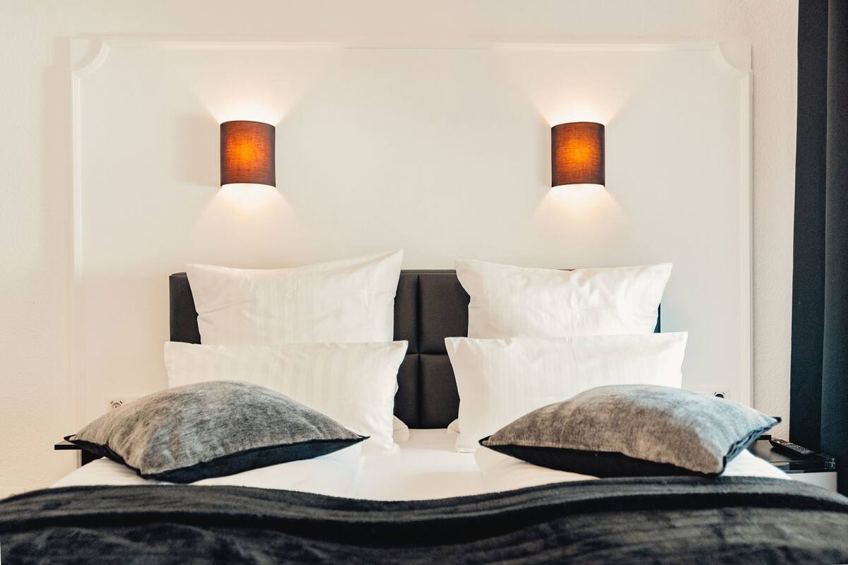 A bed with white pillows and a dark headboard, flanked by two wall-mounted lights.