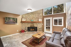 Una sala de estar con chimenea de ladrillo, televisor montado, sofá de cuero y piso con motivo de espiga.