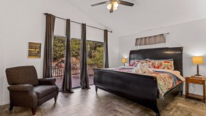 Une chambre à coucher avec un lit, une chaise, un ventilateur de plafond et une fenêtre avec des rideaux.
