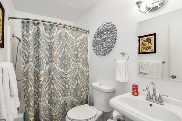 A bathroom with a shower curtain, toilet, sink, and a decorative wall piece.