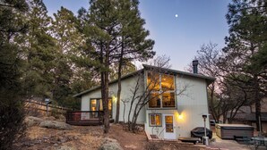 Une maison à deux étages avec une terrasse, entourée d’arbres et de rochers.