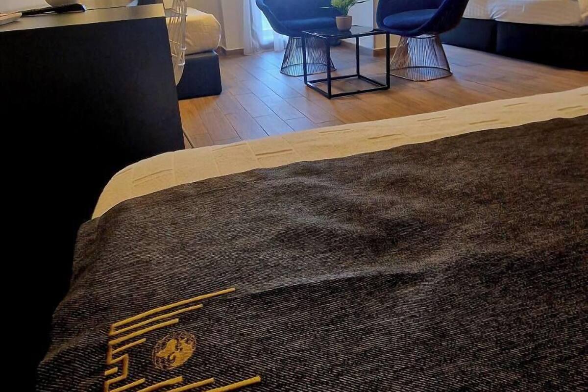 A modern hotel room with a large bed, two armchairs, a small table, and a TV mounted on the wall.