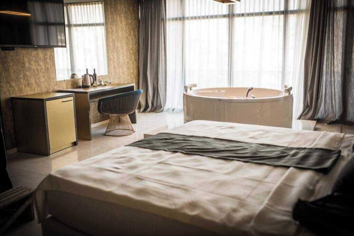 A modern hotel room with a large bed, a separate desk with a chair, a bathtub, and a television mounted on the wall.