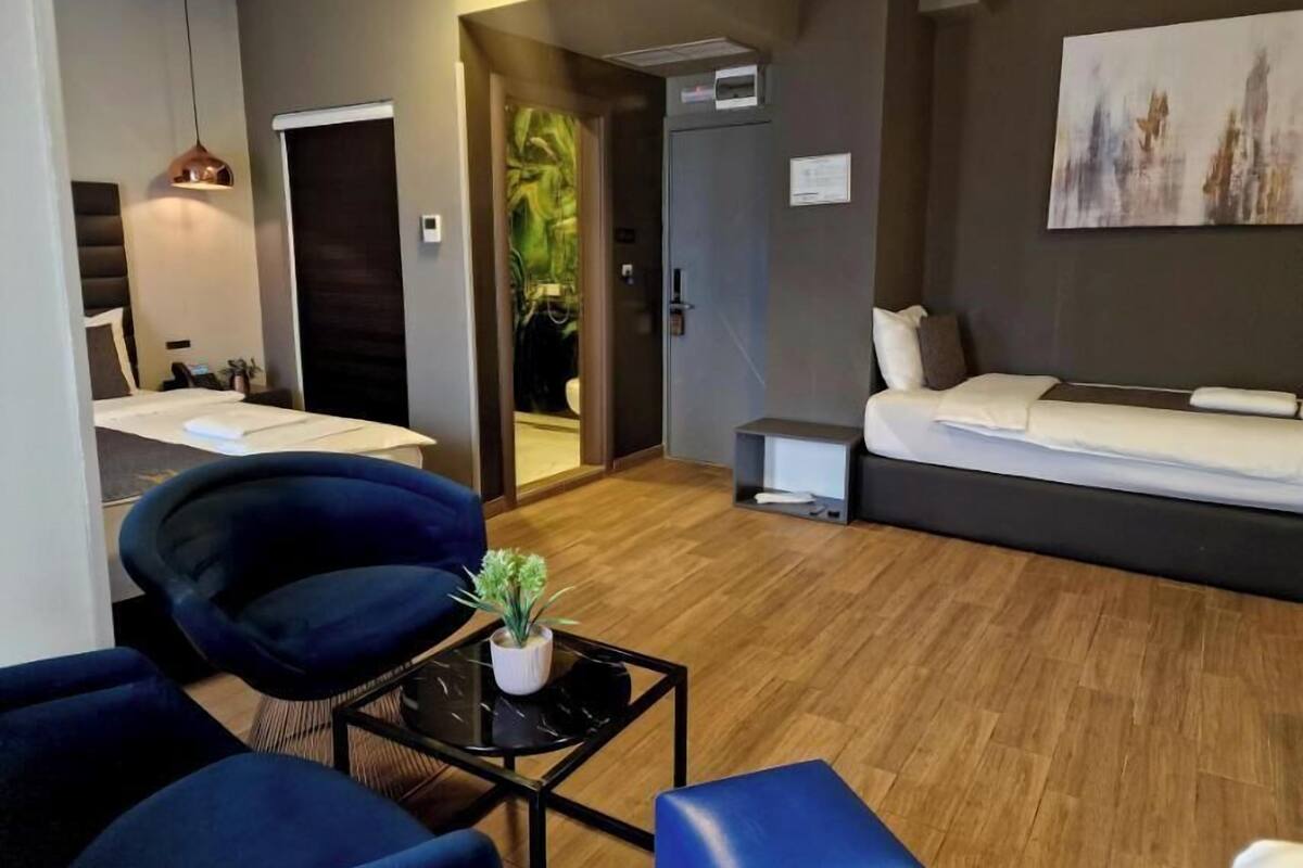 A modern hotel room with a sofa bed, a small table with a plant, a desk with a chair, and a painting on the wall.