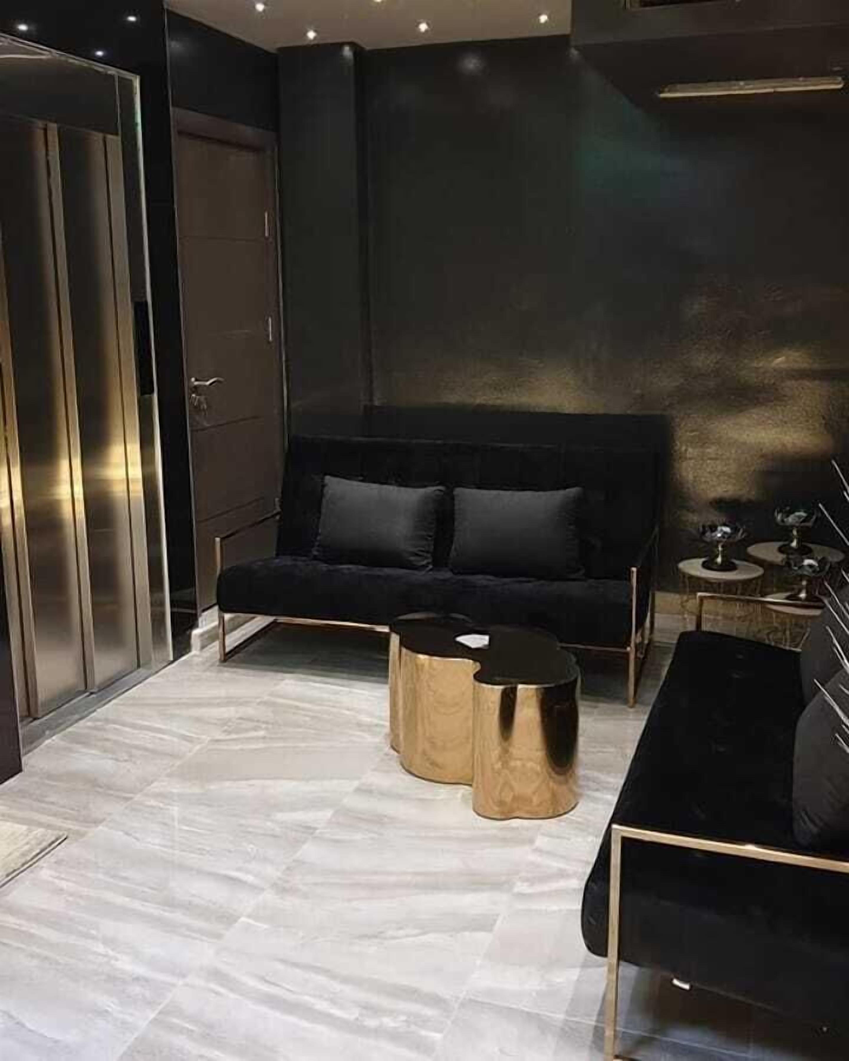 Uma sala de estar moderna com um sofá preto, duas mesas laterais douradas e uma mesa de centro preta.