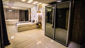 Quarto de hotel moderno com cama grande, área de estar separada, chuveiro em cabine de vidro e banheiro individual.