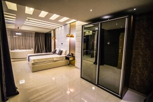 Una habitación de hotel moderna con una cama grande, un área de estar independiente, una ducha con cerramiento de vidrio y un baño separado.