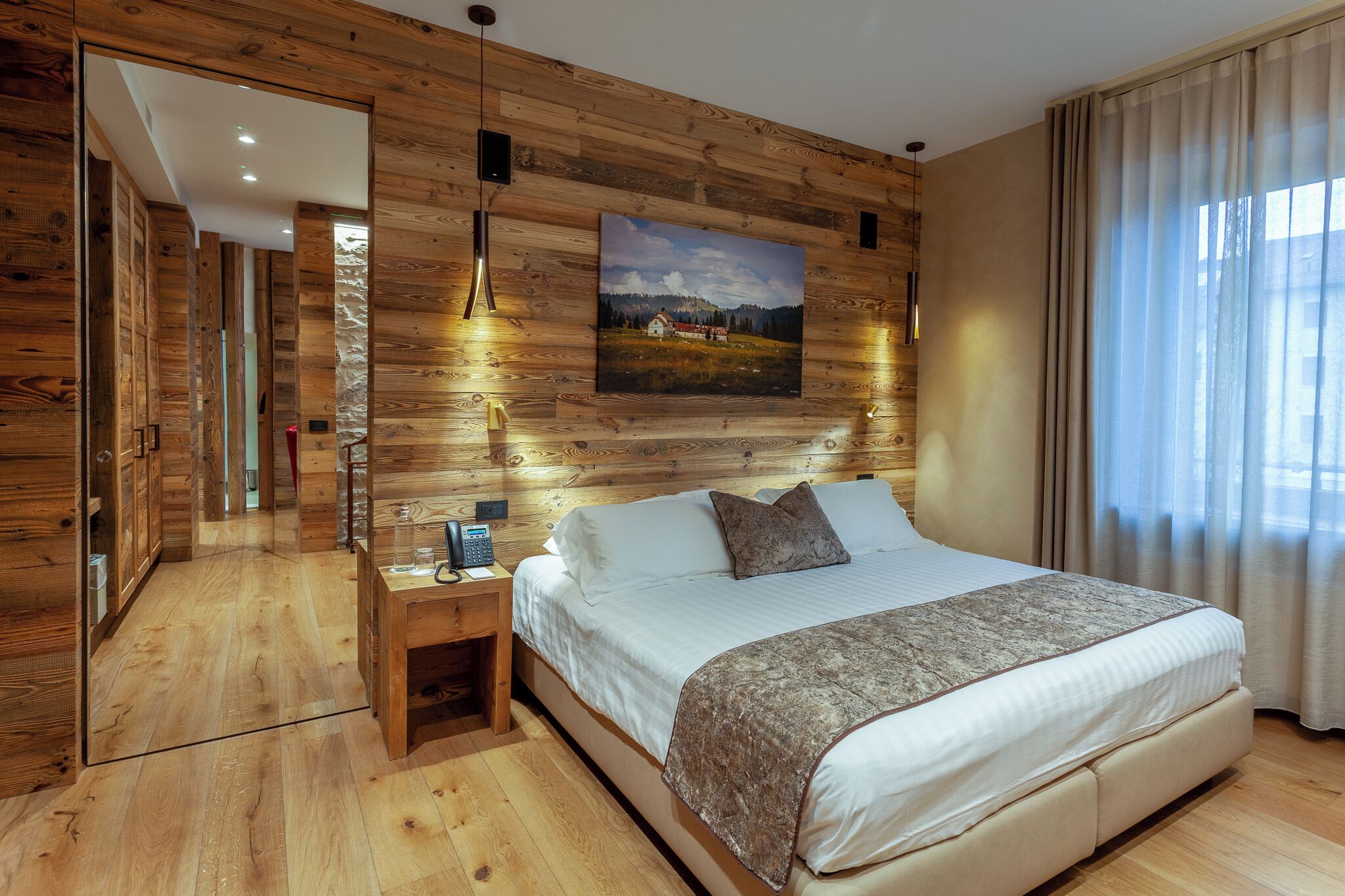 Un dormitorio con pared de madera, una cama, una mesita de noche, un cuadro y una ventana con cortinas.