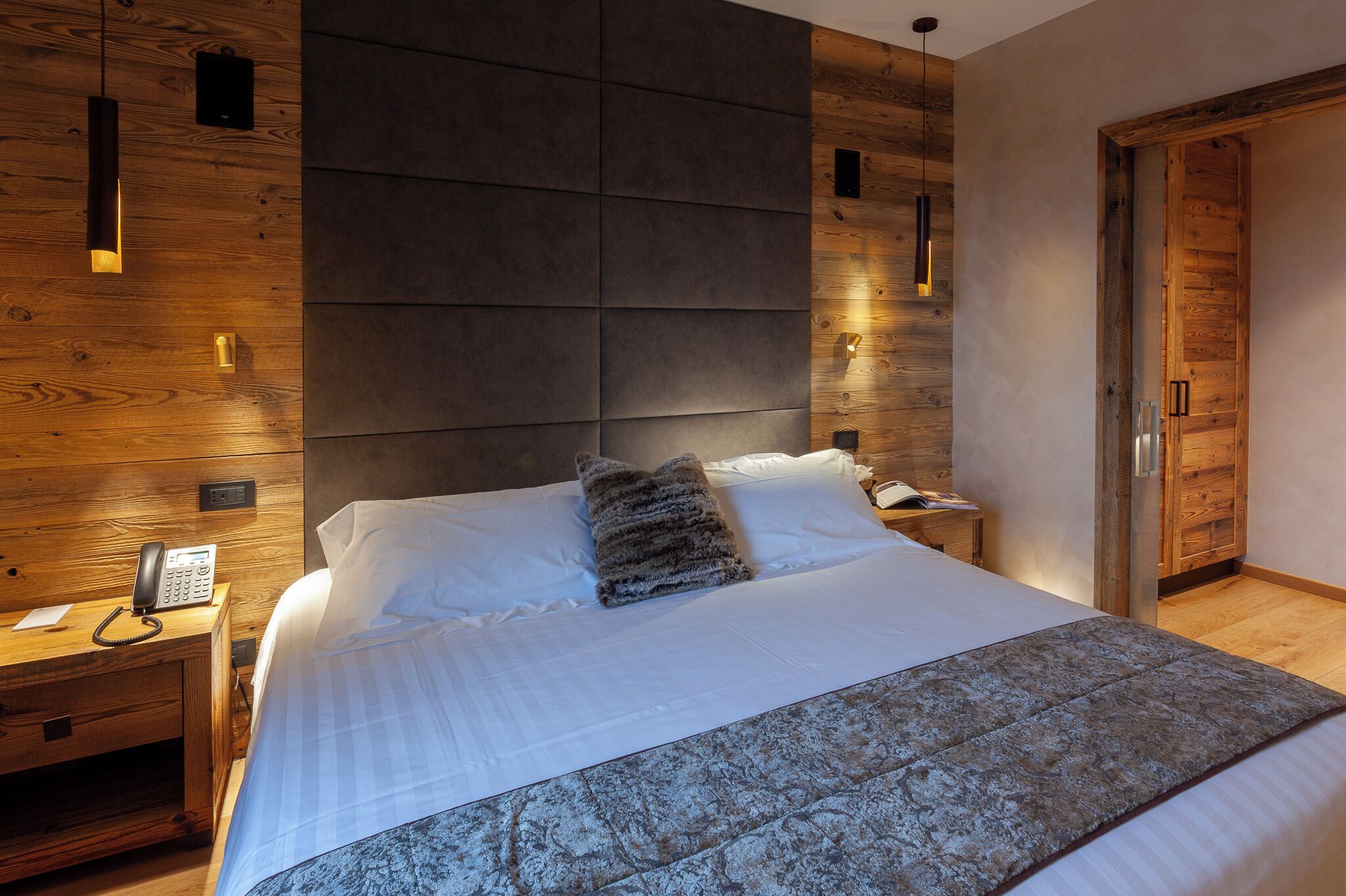 Um quarto moderno com uma cama grande, cabeceira de madeira, mesas de cabeceira com abajures e um guarda-roupa de madeira.