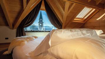 A bedroom with a bed, a window with curtains, and a view of a church steeple.