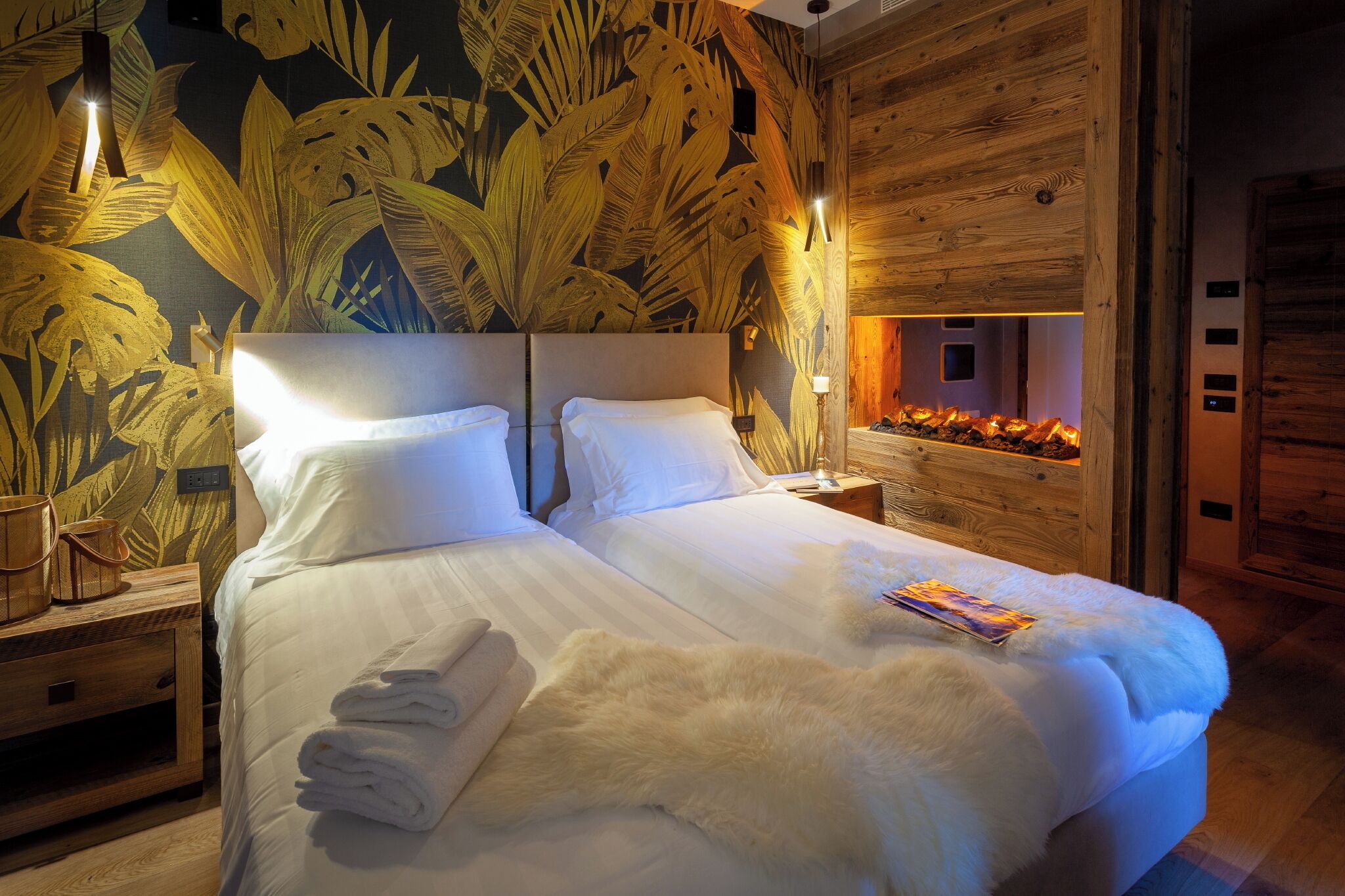 A hotel room with a large bed, wooden headboard, a wall with a tropical leaf pattern, and a nightstand with a lamp.